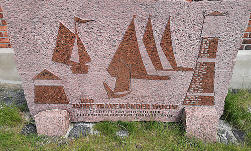Stein mit Inschrift „100 Jahre Travemünder Woche“ und Segelbooten