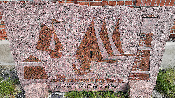 Stein mit Inschrift „100 Jahre Travemünder Woche“ und Segelbooten