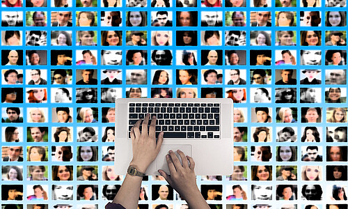 Laptop, im Hintergrund Kacheln mit Gesichtern