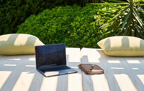 Laptop und Block auf einer Couch im Garten