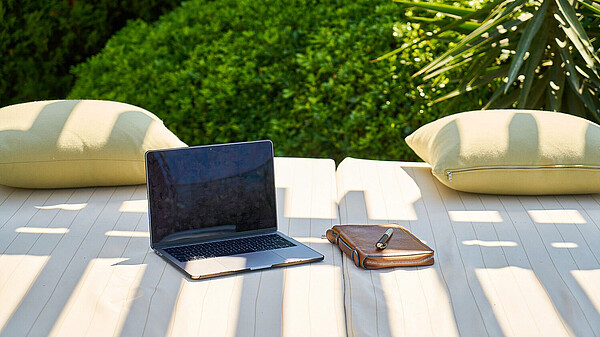 Laptop und Block auf einer Couch im Garten